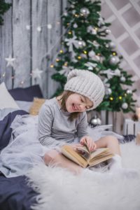Girl reading book by the Christmas tree in winter